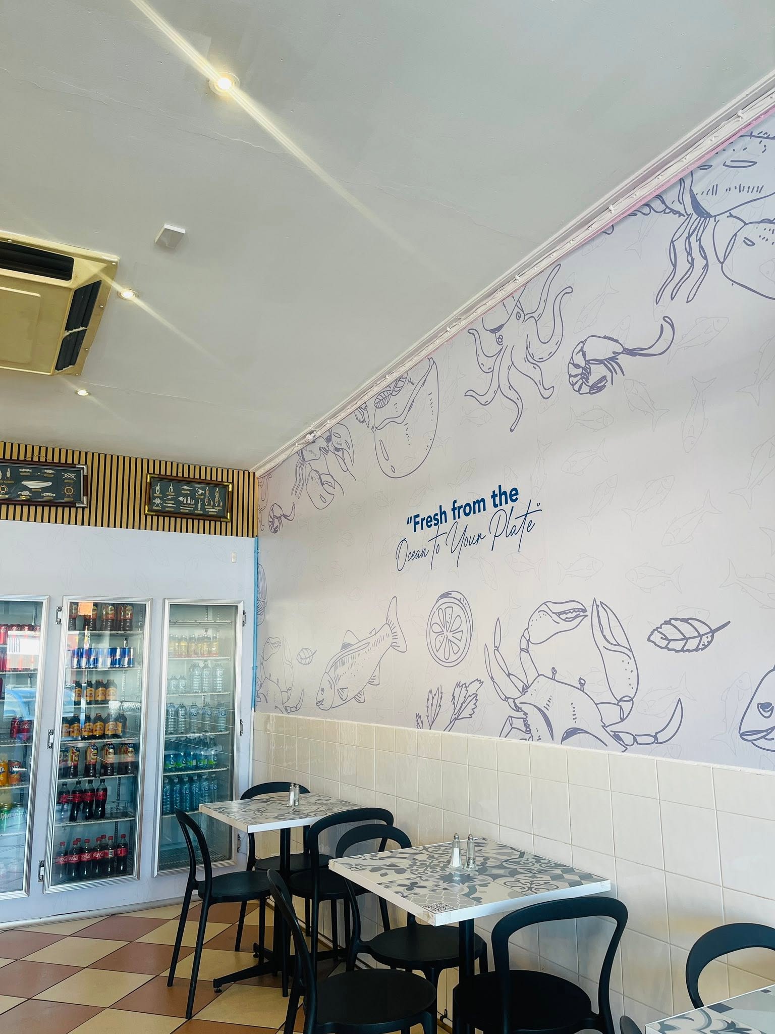 Casual dining seating inside Catch Of The Ocean with a hand-painted seafood mural on the wall